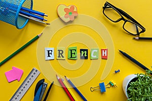 French - word made with carved letters on yellow desk with office or school supplies, stationery. Concept of Franch