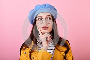 Frenchwoman lady in a stylish hat and beret and a yellow raincoat with glasses shows think on a pink background