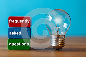 Frequently asked questions are the word written on a red and a green toy block. Next to the tow blocks, an ancient light bulb with