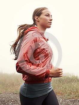 Fresh air jog. A young woman running along a road on a misty morning.