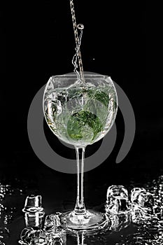 Fresh alcoholic cocktail with vodka, gin, ice, fennel in wineglass on black background. Studio shot of drink in freeze motion,