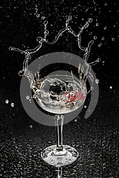 Fresh alcoholic cocktail with vodka, gin, ice, flower in wineglass on black background. Studio shot of drink in freeze motion,