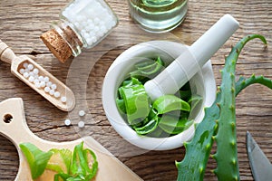 Fresh aloe vera leaves, mortar full of chopped aloe and bottle of homeopathy globules.