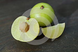 Fresh Amla Berry Cross Section with Whole Fruit on Black Wooden Background