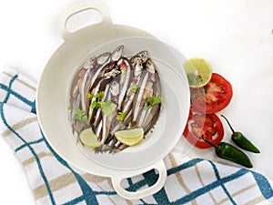 Fresh Anchovy Fish decorated with herbs and vegetables on a white background.