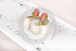 Fresh appetizer with pita bread roll,  with cream cheese,  ham and green vegetables,  decorated with tomato and green leaf,