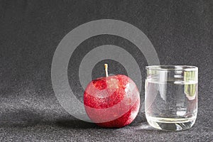 Fresh apple with glass of clean drinking water over gray background
