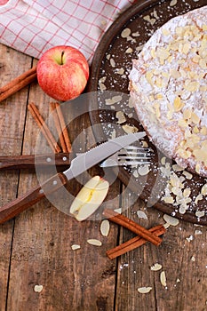 Fresh apple pie with cinnamon sticks and fresh apples on a plate on brown rustic wooden table