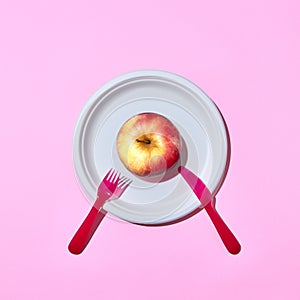 Fresh apple on a plate served with plastic knife and fork