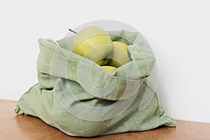 Fresh apples in eco cotton bag on wooden table. Zero waste shopping. Fruits in reusable green bag