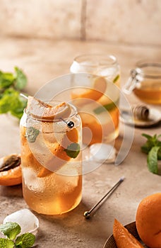 Fresh apricot cocktail, fizz or ice tea with mint and garnish. Pink beige tile background