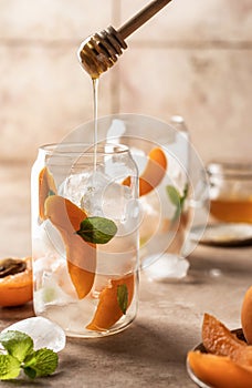 Fresh apricot cocktail, fizz or ice tea with mint and garnish, process of adding honey. Pink beige tile background