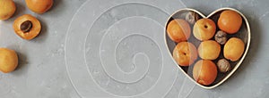 Fresh apricots in wooden heart shaped box, on gray background. Fruit banner. Copy space.