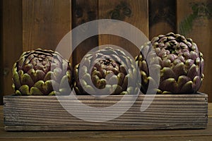 3 fresh artichokes green-purple flower head, on wooden background