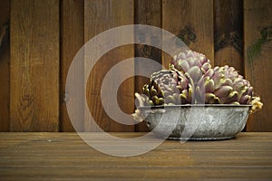 3 fresh artichokes green-purple flower head, on wooden background