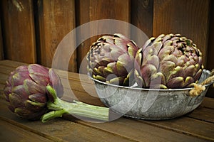 3 fresh artichokes green-purple flower head, on wooden background