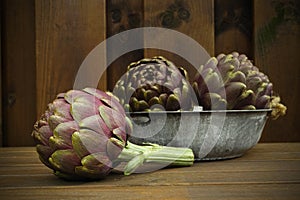 3 fresh artichokes green-purple flower head, on wooden background