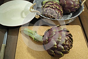 Fresh artichokes green-purple flower heads, on wooden background