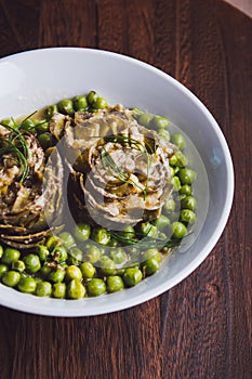 Fresh artichokes with parsley and young beans in a baking pan, parmesan in background.