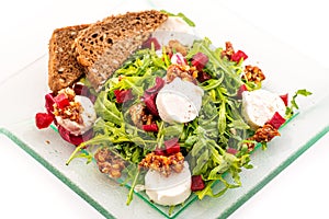 Fresh arugula salad with beetroot, goat cheese, bread slices and walnuts on glass plate isolated on white background, product