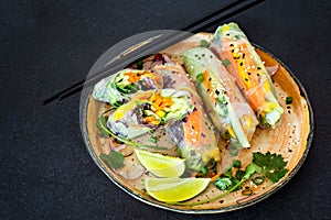 Fresh Asian appetizer Spring rolls Nem made from rice paper and raw vegetables and herbs with hot sauce on a dark background.