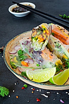 Fresh Asian appetizer Spring rolls Nem made from rice paper and raw vegetables and herbs with hot sauce on a dark background.