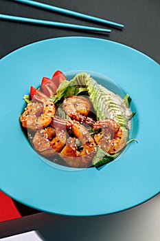 Fresh asian green salad with avocado, shrimps, tomatoes , red bell peper and nut sauce in blue color boul at colorful background