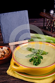 Fresh asparagus creamy soup and ingredients on a wooden table.