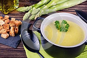 Fresh asparagus creamy soup and ingredients on a wooden table.