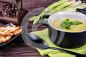 Fresh asparagus creamy soup and ingredients on a wooden table.