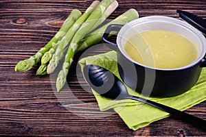 Fresh asparagus creamy soup and ingredients on a wooden table.