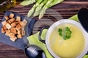 Fresh asparagus creamy soup and ingredients on a wooden table.