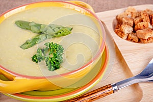 Fresh asparagus creamy soup and ingredients on a wooden table.