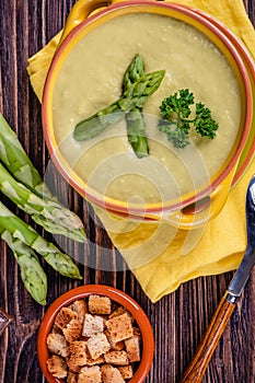 Fresh asparagus creamy soup and ingredients on a wooden table.