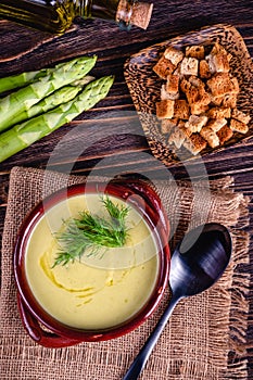 Fresh asparagus creamy soup and ingredients on a wooden table.