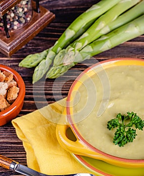 Fresh asparagus creamy soup and ingredients on a wooden table.