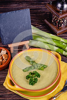 Fresh asparagus creamy soup and ingredients on a wooden table.