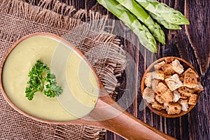 Fresh asparagus creamy soup and ingredients on a wooden table.