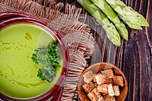 Fresh asparagus creamy soup and ingredients on a wooden table.