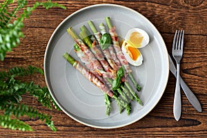 Fresh asparagus wrapped in bacon and grilled, served with egg benedict. Healthy food.