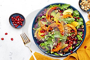 Fresh autumn pumpkin salad with baked pumpkin slices, red cabbage, avocado, arugula, pomegranate seeds and walnuts. Healthy vegan