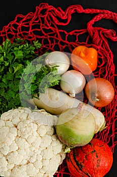 Fresh autumn vegetables on red reusable mesh bag on black background. Zero waste concept. Flat lay. Top view