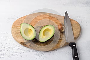 Fresh avocado cut in half and avocado pit with a knife on a wooden board on a light gray background, top view