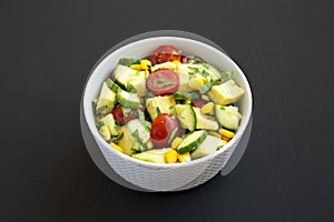 Fresh Avocado Tomato Salad in a bowl on a black background, side view