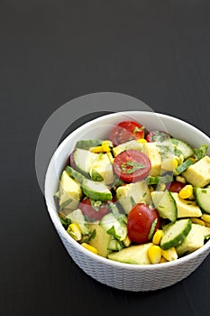 Fresh Avocado Tomato Salad in a bowl on a black background, side view. Copy space