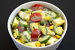 Fresh Avocado Tomato Salad in a bowl on a black surface, side view. Close-up