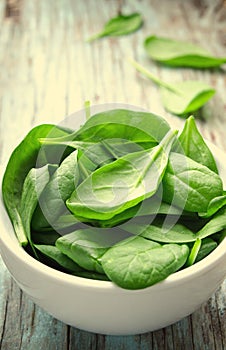 Fresh Baby spinach leaves in white bowl on blue wooden background. Top view with copy space, horizontal. Healthy