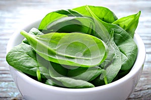 Fresh Baby spinach leaves in white bowl on blue wooden background. Top view with copy space, horizontal. Healthy