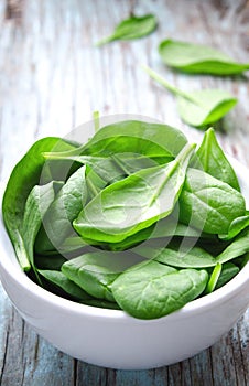 Fresh Baby spinach leaves in white bowl on blue wooden background. Top view with copy space, vertical. Healthy, Ecology