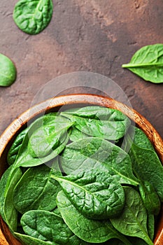 Fresh baby spinach leaves in wooden bowl on rustic stone table top view. Organic healthy food.